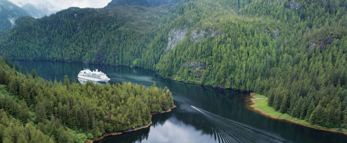 Photo from Seabourn Quest of their Alaskan Cruise. Cruise ship in dark blue waters surrounded by green mountains in Alaska.